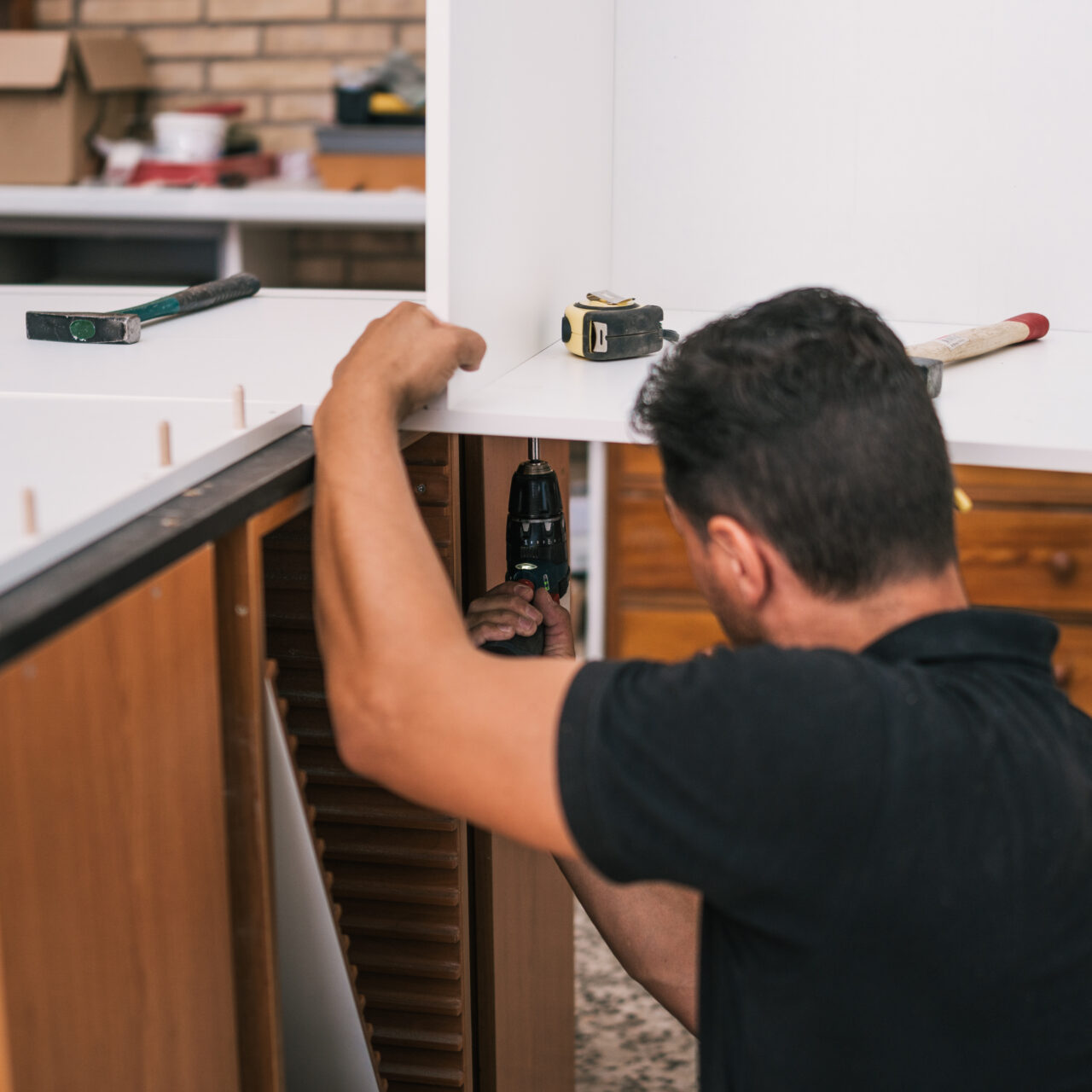 Worker using a drill to put together two perpendicular pieces of kitchen furniture in a workshop